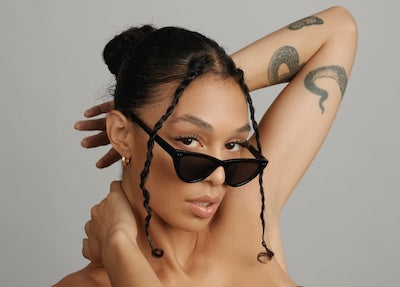 Woman wearing sunglasses with long lash extensions, one arm raised behind her head.